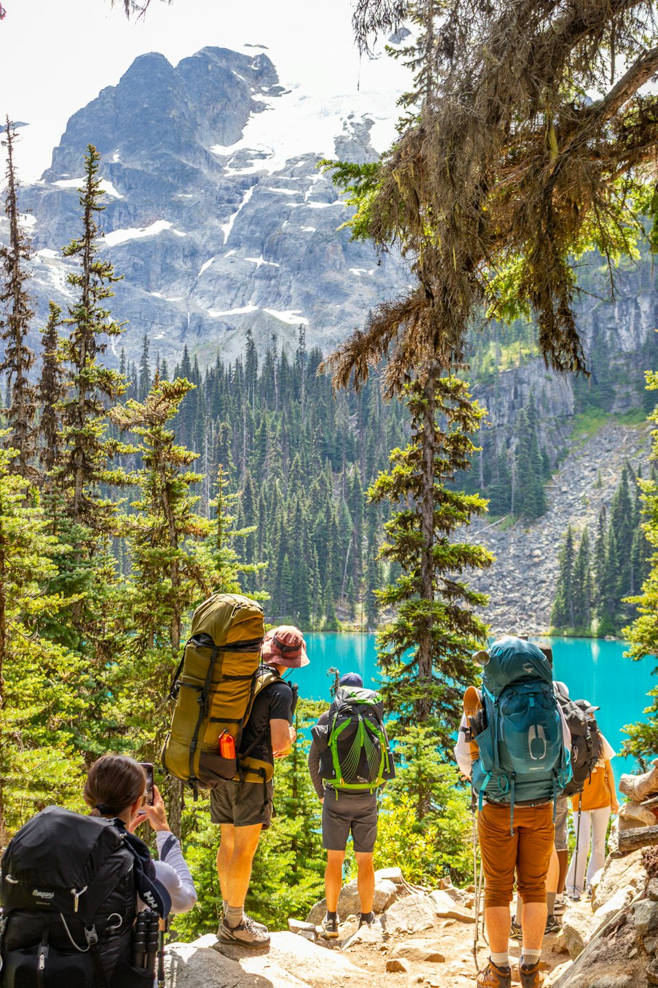 Senderistas con mochilas observan un lago turquesa y una cordillera.